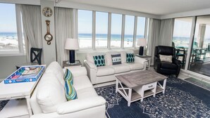 Un salón amplio con un sofá blanco, una mesita de centro y vista a la playa a través de ventanas grandes.