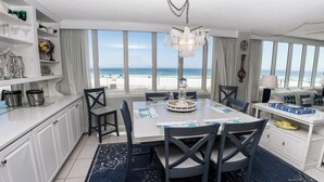 Comedor con vistas a la playa, muebles blancos y una araña.