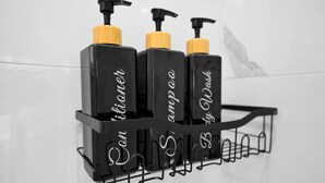 Une étagère noire dans la salle de bain, sur laquelle sont posées trois bouteilles de shampoing et d’après-shampoing.