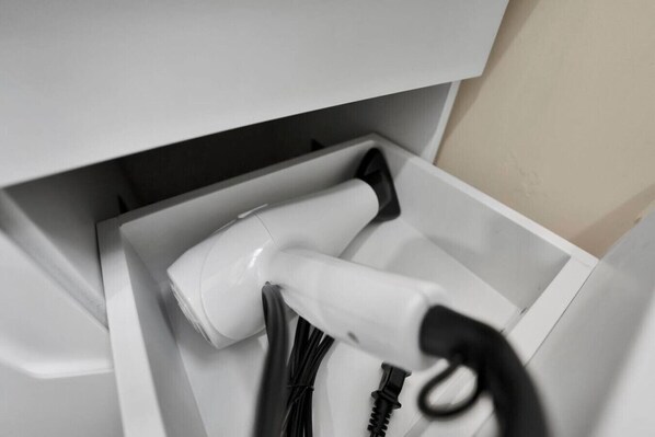 A white hairdryer in a drawer with a black cord.