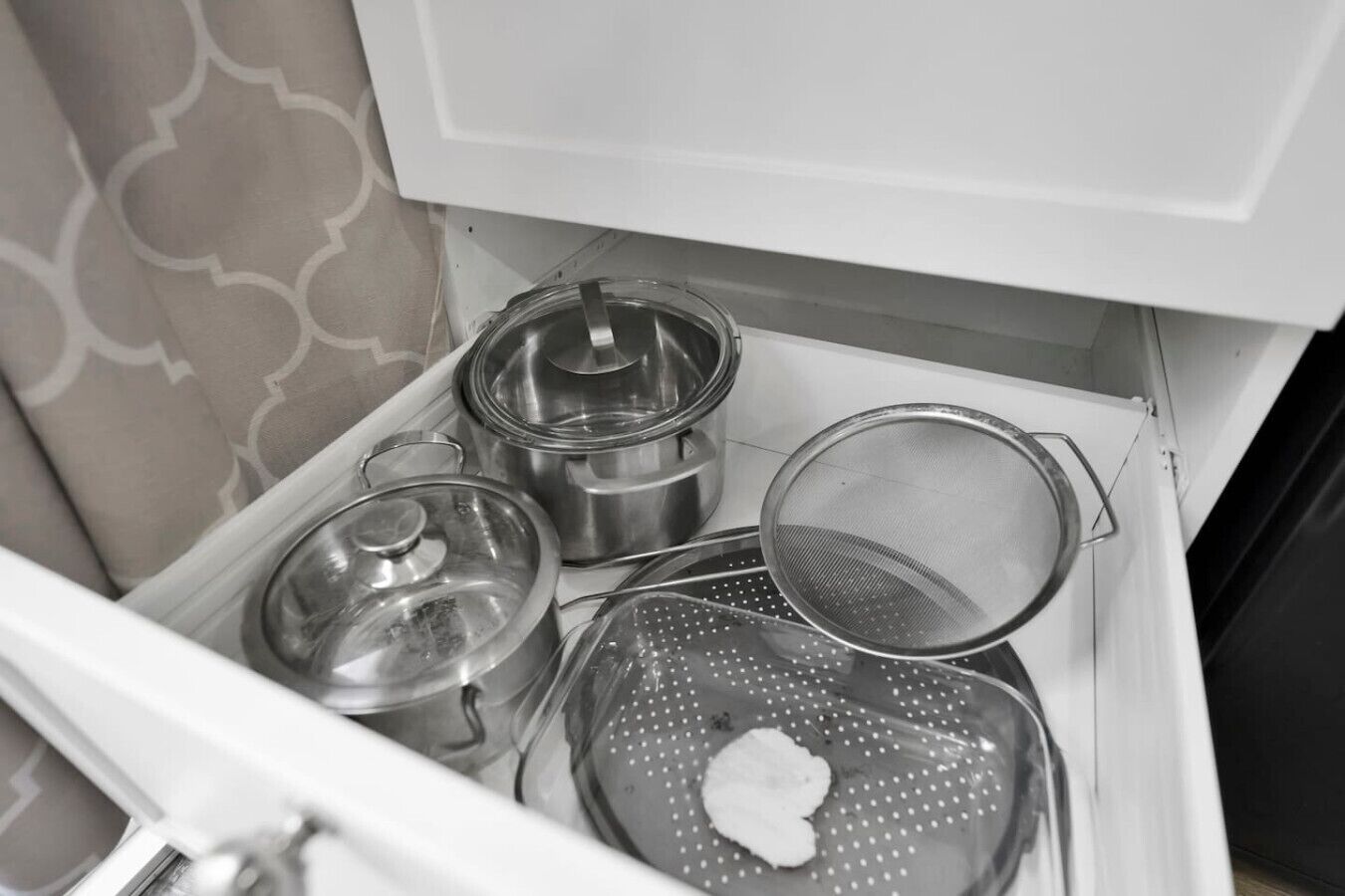 Un cajón de cocina con ollas de acero inoxidable, un colador y un escurridor.
