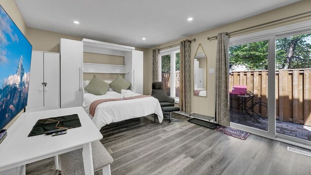 Une chambre à coucher comprenant un lit, une table de chevet, une chaise et donnant sur l’extérieur.