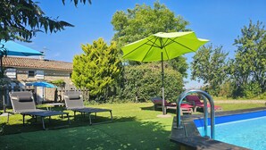 Un patio trasero con piscina, césped verde y sillones de descanso.