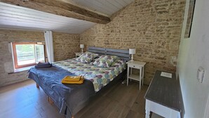 Un dormitorio con techo de madera, una cama con colcha estampada, una mesita de noche con lámpara y una ventana con cortinas.