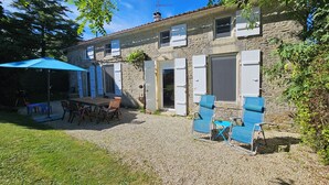 Una casa de piedra con un patio de grava, mobiliario exterior y un paraguas azul.