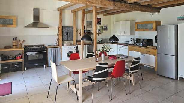 Una cocina con vigas de madera, una estufa, una lavadora y un comedor con sillas.