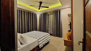 A hotel room with a bed, curtains, a ceiling fan, and a bedside table with a clock. - Staycation At Sandari Batulao (Overlooking Spot) (Tagaytay)