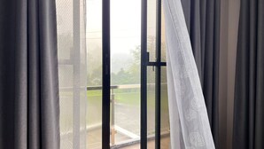 A view through a window with grey curtains, a mesh screen, and a white sheer curtain with leaf patterns. - Staycation At Sandari Batulao (Overlooking Spot) (Tagaytay)
