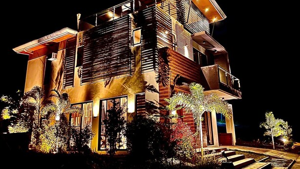 A modern multi-story building with a prominent staircase, large windows, and a well-lit facade. - Staycation At Sandari Batulao (Overlooking Spot) (Tagaytay)