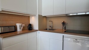 A modern kitchen with white cabinets, a wooden countertop, a toaster, a kettle, a coffee maker, a sink, and a dishwasher. - Aux Angles apartment, lake view, 5 minutes walk from the village center! (Les Angles)