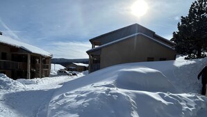A snow-covered street with buildings, including a two-story structure with a balcony and a smaller building with a sloped roof. - Aux Angles apartment, lake view, 5 minutes walk from the village center! (Les Angles)