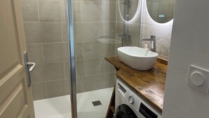 A bathroom with a glass shower enclosure, a white sink with a wooden countertop, and a washing machine. - Aux Angles apartment, lake view, 5 minutes walk from the village center! (Les Angles)