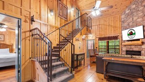 L’intérieur d’un chalet en bois, avec un escalier, une cheminée et une table de billard.