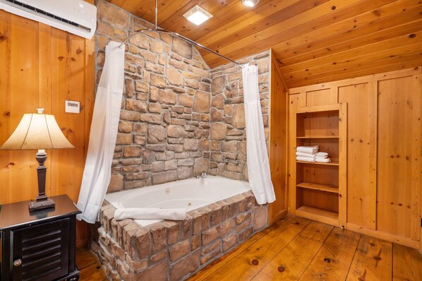 Un baño con paredes de piedra, una bañera, un armario de madera y una lámpara.