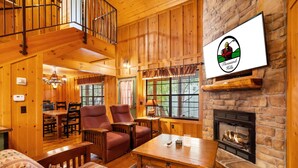 A cozy log cabin interior with a fireplace, wooden furniture, and a dining area.