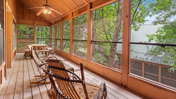 A wooden deck with rocking chairs and large windows overlooking a forest.