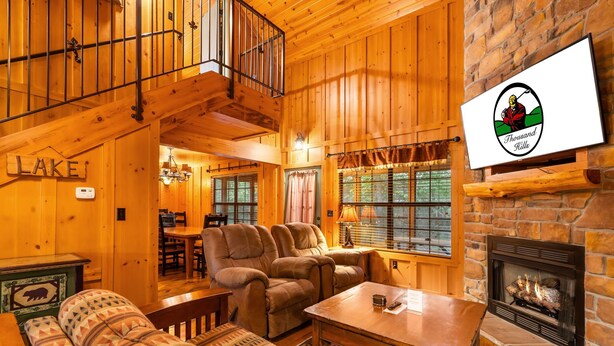 A cozy cabin interior with a fireplace, wooden walls, a sofa, and a dining area.