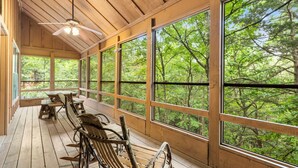 A wooden deck with benches and a ceiling fan, large windows offering a view of a forest.