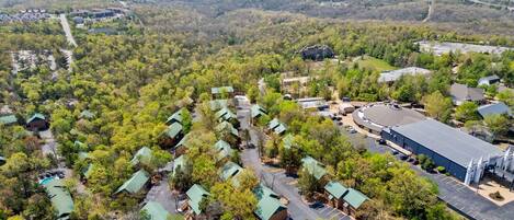 An aerial view of a resort with multiple green-roofed cabins, a large building with a flat roof, and a parking area.