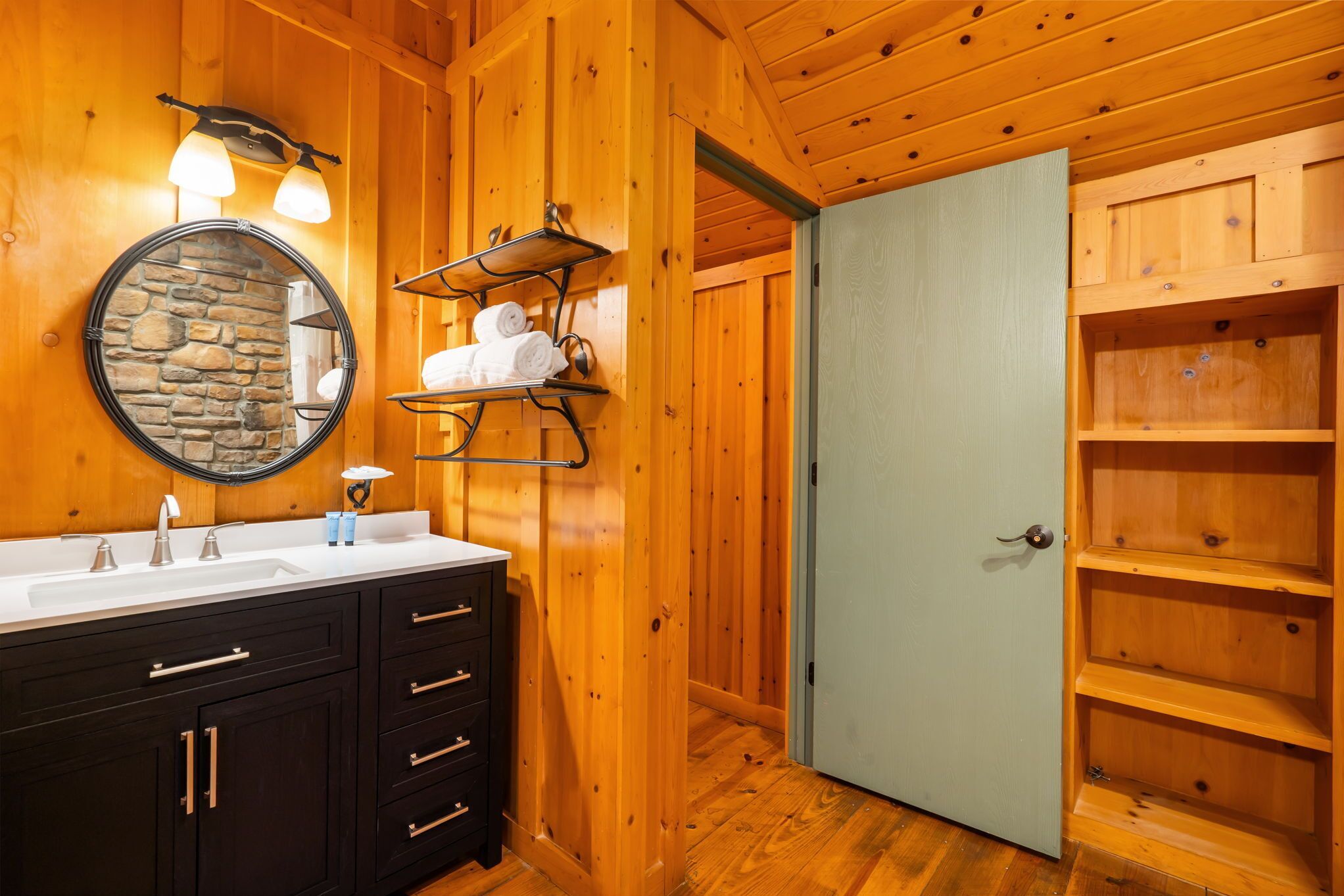A wooden bathroom with a double sink, a stone wall mirror, and a towel rack.