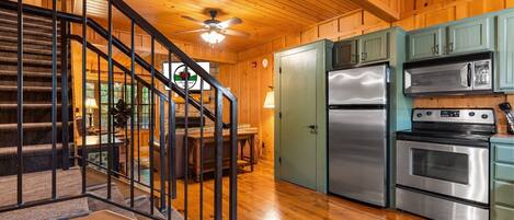 A wooden interior with a staircase, a ceiling fan, a dining area, and kitchen appliances.