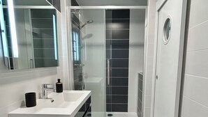 Une salle de bain moderne avec un lavabo blanc, un meuble-lavabo noir et une cabine de douche en verre.