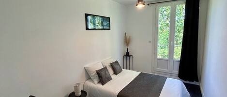 Une chambre à coucher comprenant un lit, une table de chevet, une lampe, une fenêtre avec des rideaux et un luminaire suspendu.