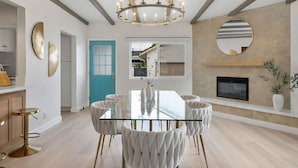 A modern dining area with a glass table, tufted chairs, a chandelier, and a fireplace.