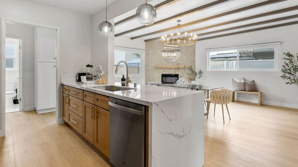 A modern kitchen with wooden cabinets, a marble island, and pendant lighting.