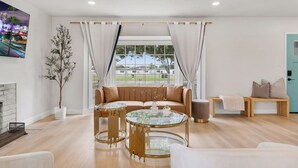 A modern living room with a sofa, a glass coffee table, and a view of a building through large windows.