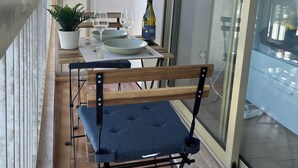 En balkon med spisebord, stole, en vinflaske og en potteplante.