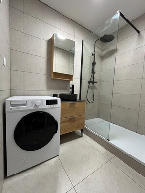 Une salle de bain moderne équipée d’un lave-linge, d’un meuble en bois et d’une cabine de douche en verre.