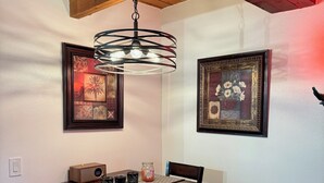 A dining area with a wooden table, four chairs, a woven placemat, a speaker, and two framed artworks on the wall.