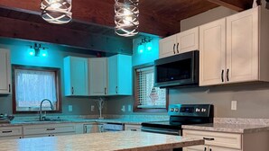 A kitchen with white cabinets, a granite countertop, a microwave, and two red bar stools.