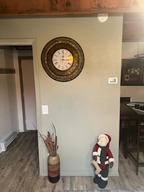 Una habitación con un reloj en la pared, un jarrón decorativo con plantas secas y un peluche.