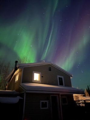 A house with a snow-covered roof and a window lit from inside. - Quiet North Pole Stay near Santa and FAI with Arctic Spa (North Pole)