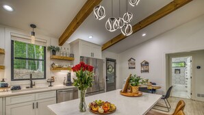 A modern kitchen with white cabinetry, a central island with a fruit platter, a vase with red flowers, and a hanging light fixture.