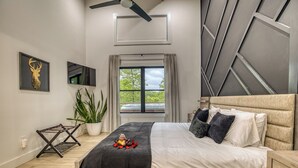 A modern bedroom with a bed, a ceiling fan, a window with curtains, a plant, and a wall-mounted TV.