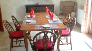 A dining table set for six with red cushions, a dark wooden cabinet, and a beige armchair in the background.