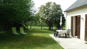 A patio with a table and chairs, a covered table, and a lawn.