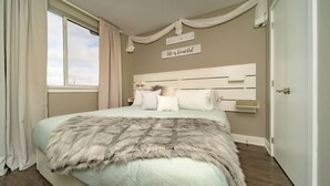 A bedroom with a large bed, a headboard with a quote, a window with curtains, and a door. - 12 Condo/King Bed/Close To  Attractions/Laundry (Niagara Falls)