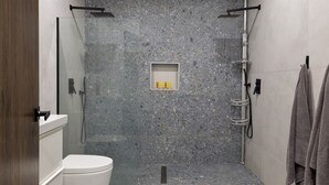 A modern bathroom with a glass shower enclosure, a toilet, and a shelf with toiletries.