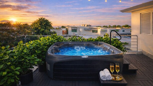 Terraza en la azotea con jacuzzi, plantas en macetas y una mesa con toallas y una copa de champán.