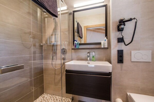 A modern bathroom with a glass-enclosed shower, a white sink with a dark cabinet, a large mirror, and a hairdryer mounted on the wall. - Chalet With Sauna and Natural Pool (Neukirchen am Grossvenediger)