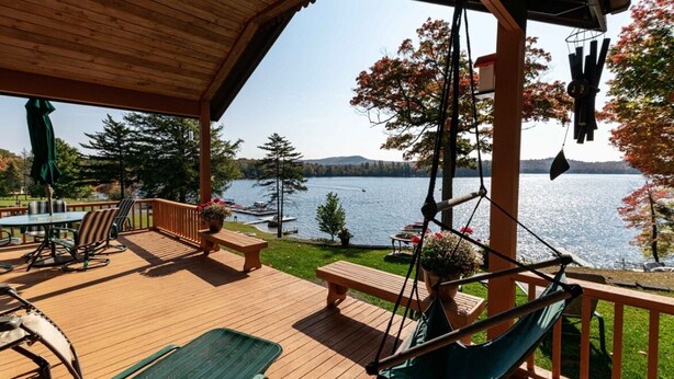 A wooden deck with outdoor furniture, a hammock, and a view of a lake and trees.