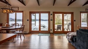 A spacious room with a wooden dining table and chairs, a sofa, and large sliding glass doors leading to a snowy outdoor area.