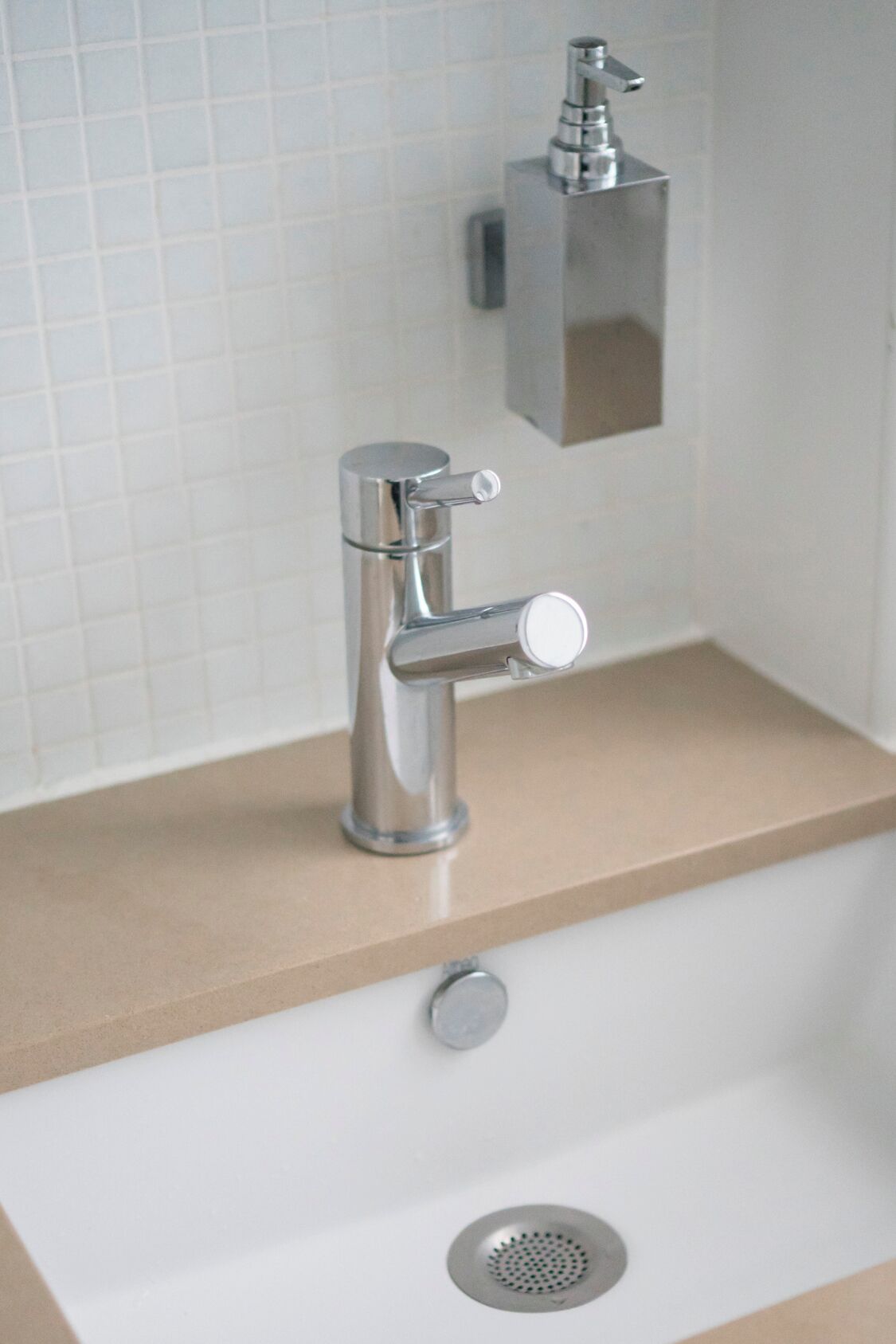 A modern bathroom with a chrome faucet, a soap dispenser, and a drain.