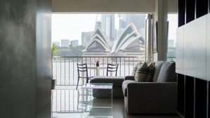 A modern living room with a sofa and chairs, a glass coffee table, and a view of the Sydney Opera House.