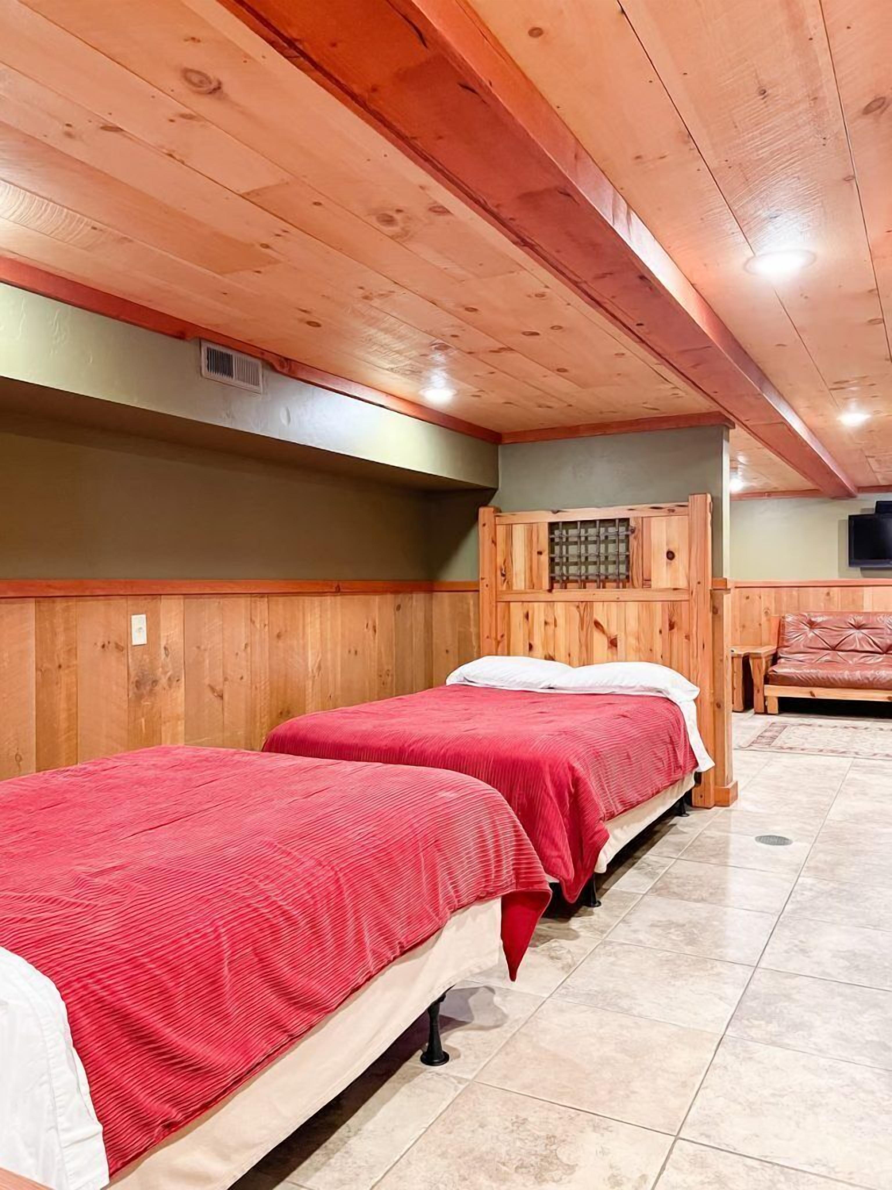 Une chambre avec deux lits, des murs en bois, une armoire en bois et un canapé en cuir.