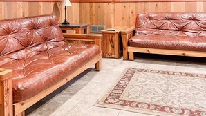 A cozy room with wooden paneling, a flat-screen TV mounted on the wall, two leather sofas, a small table, and a patterned rug. - Club 51 (Mercer)